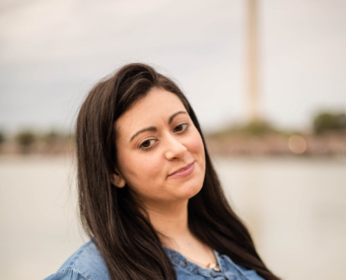 Photo of Jennifer Heiser with the Washington Monument blurry in the background. Jennifer is wearing a jean top with her hair down.